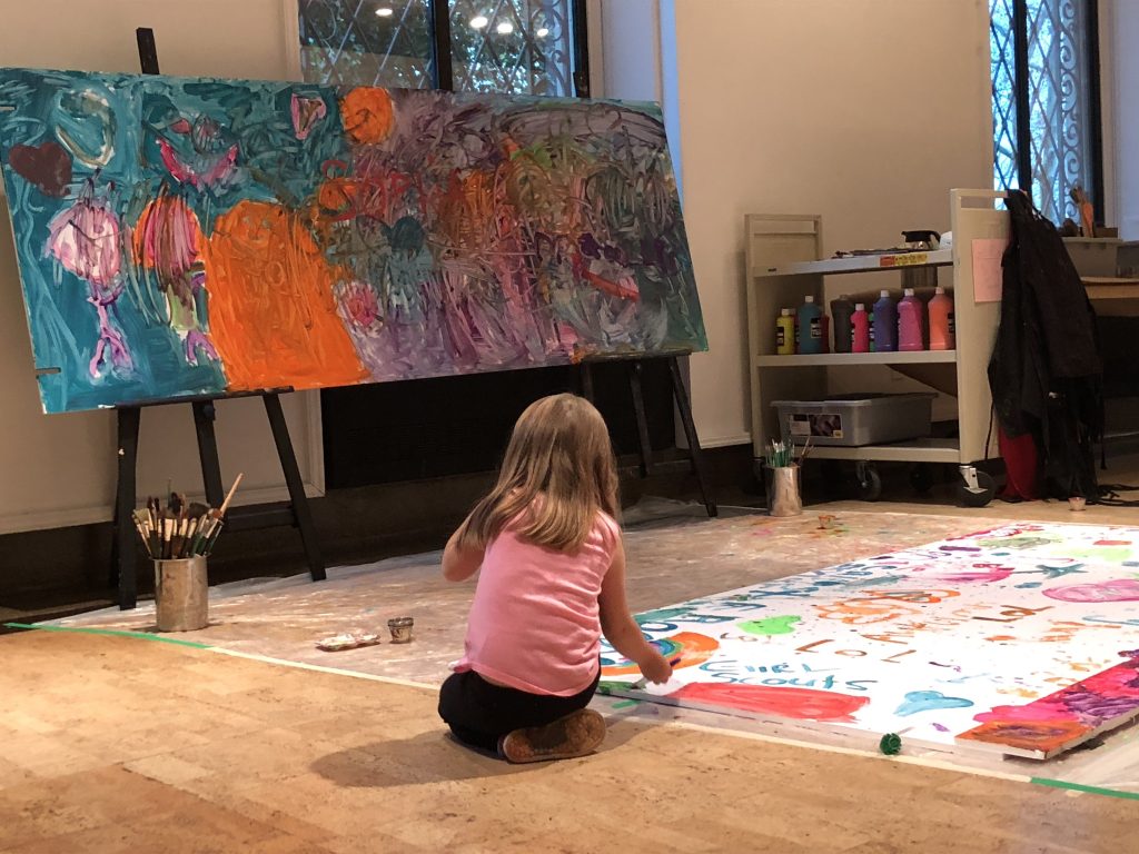 little girl sitting on the floor painting photographed from behind